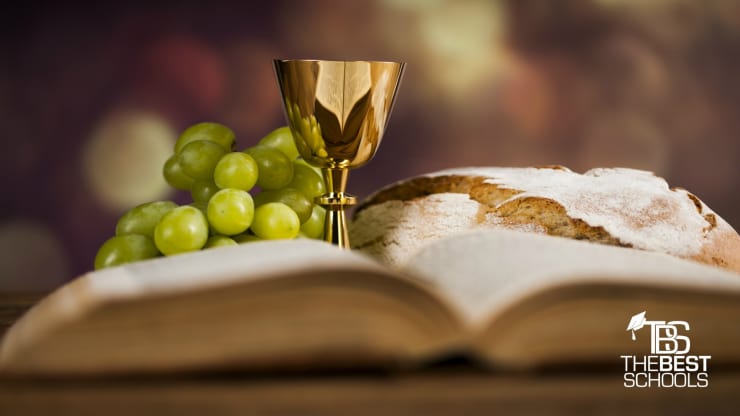 The Best Online Associate in Theology Programs Hero Image: Best Online Associate in Theology Programs (image of an open Bible displayed before a bunch of grapes, a loaf of bread, and a golden goblet)