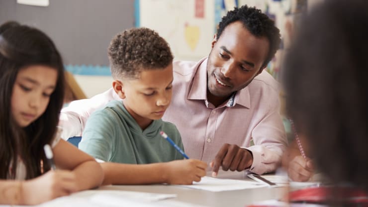 The Most Affordable Online Master's in Early Childhood Education Degree Programs Hero Image: The Most Affordable Online Master's in Early Childhood Education Degree Programs (Image of a teacher instructing young students on a worksheet)