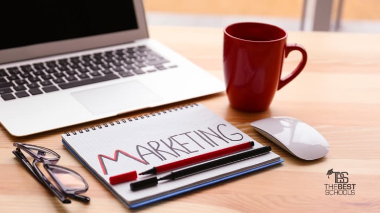 Hero image for What Can You Do With a Marketing Degree?: Image of Desk with a laptop computer, a coffee mug, and a notebook that has Marketing written on it