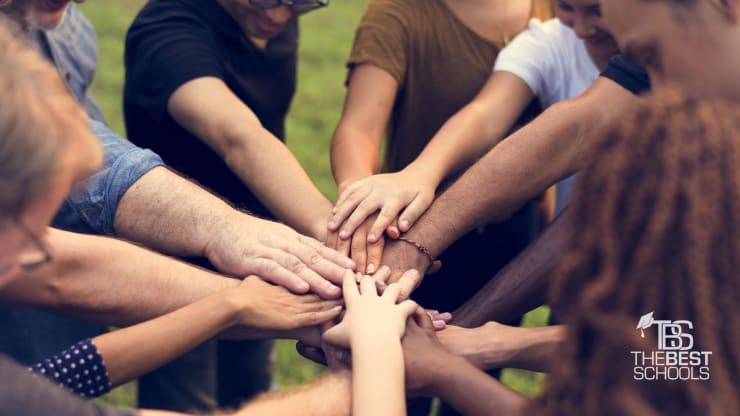 Image of people in a circle placing their hands over each other’ hands