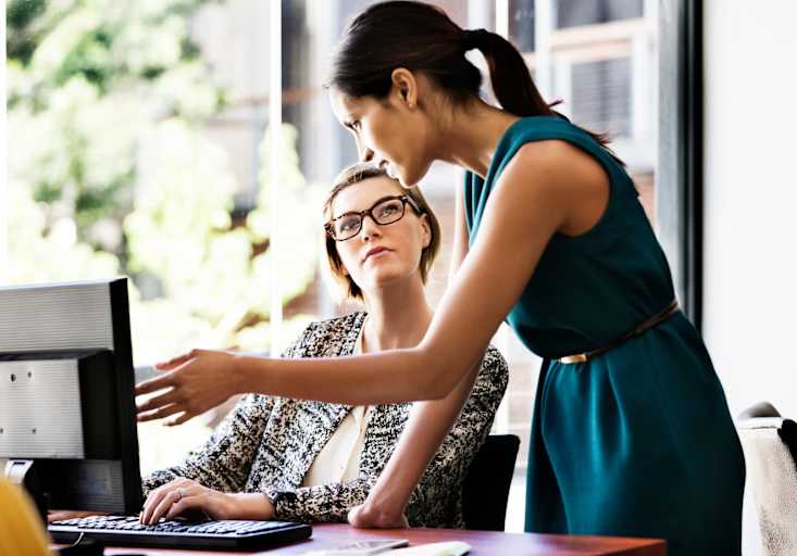 Two women working together on a computer in an office
