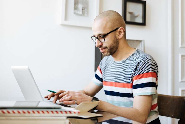 Bald man sitting on a desk at home and working on his laptop.