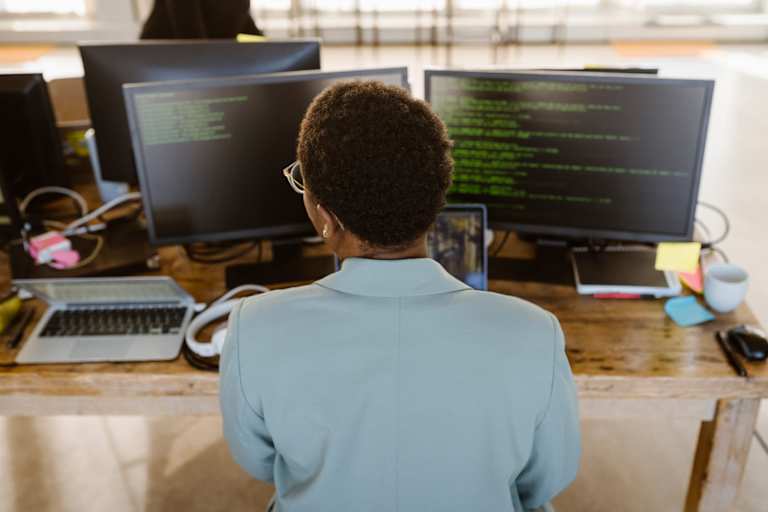 Rear view of female programmer working on computer at desk in creative office