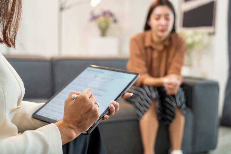 Psychologist speaking to patient while taking notes on tablet