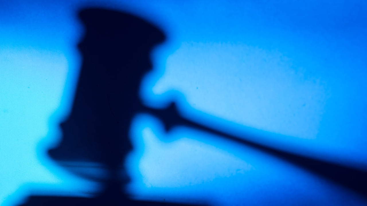 A faded silhouette of a judge's gavel resting on a bench in a courthouse.