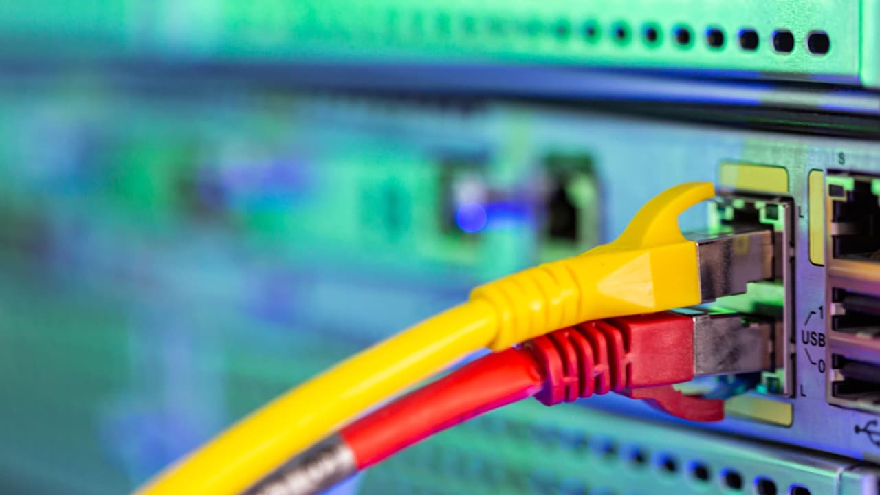 Close-up on the pair of yellow and red Ethernet cables plugged in the panel of telecommunication server. Selective focus shot with blurred background copy space