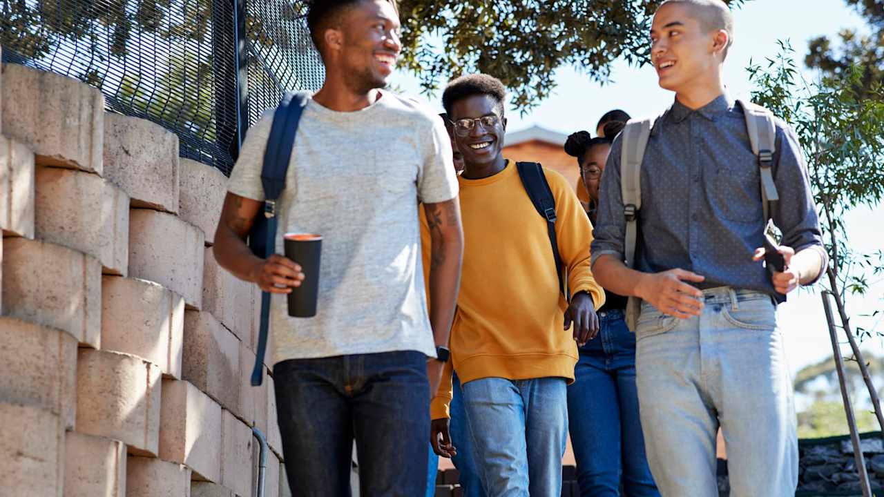 Low angle view of smiling young multi-ethnic friends moving down on staircase by wall