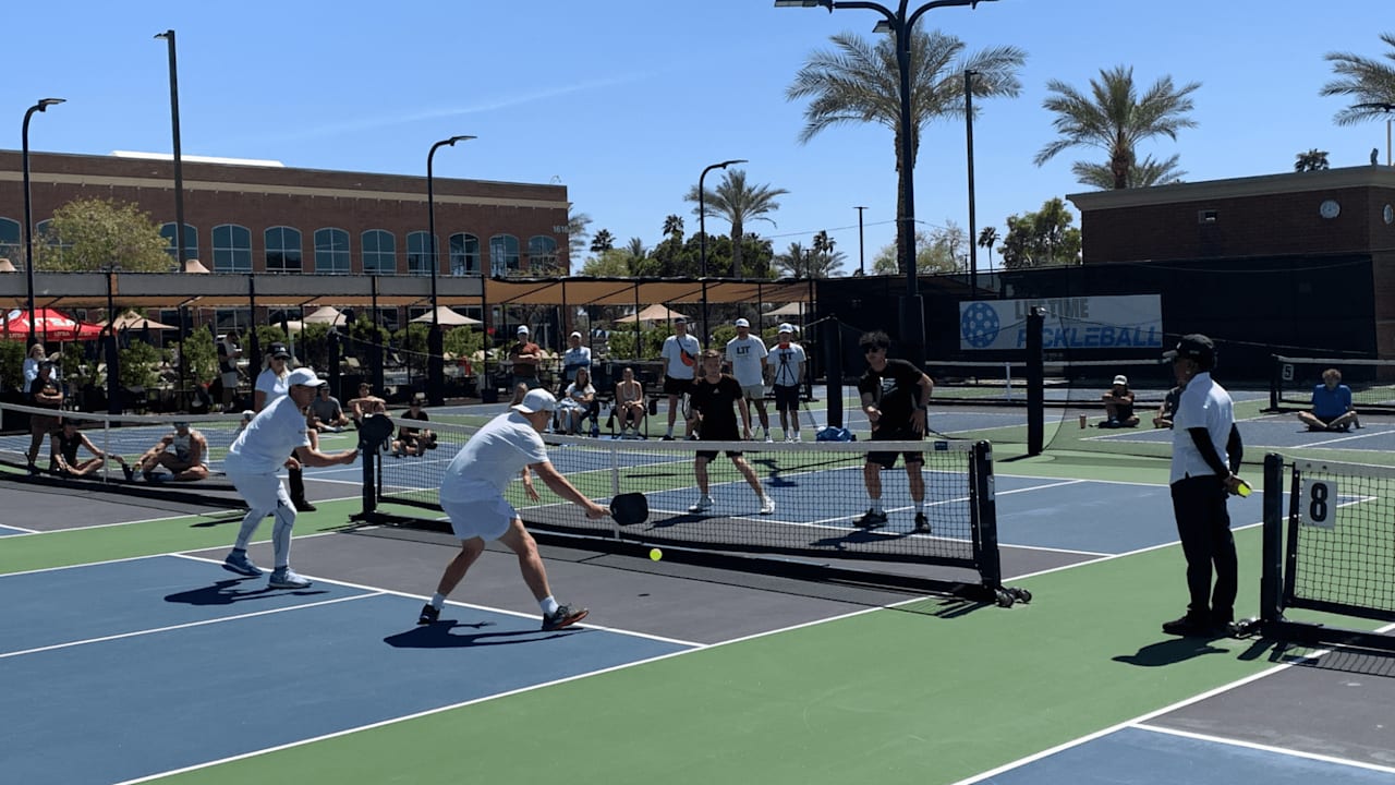 A group of people wearing white clothing playing pickleball on a bright sunny day.