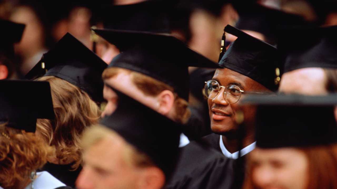 Graduates at graduation ceremony (focus on young man in glasses)
