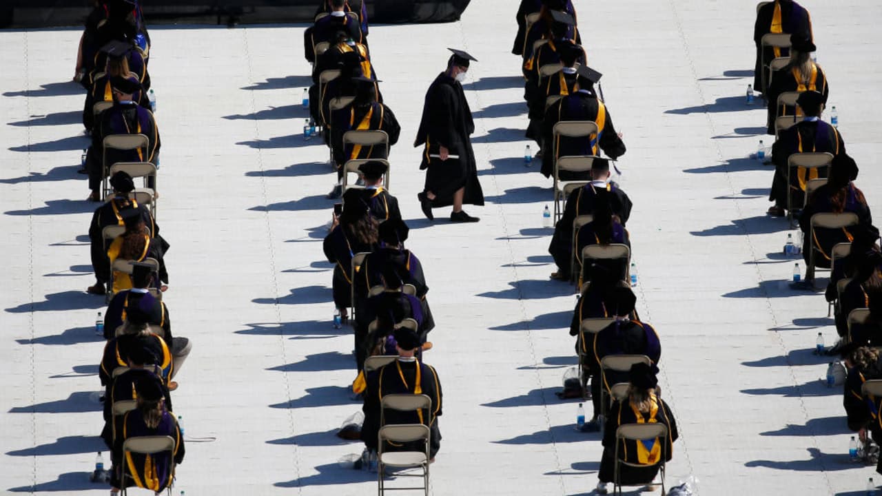 A graduate carries his diploma as he walks between rows of socially distanced colleagues