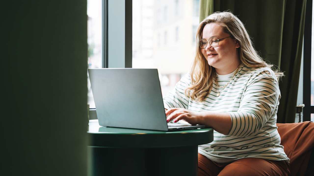 Caucasian female college student in casual clothes working on her laptop in a cafe.