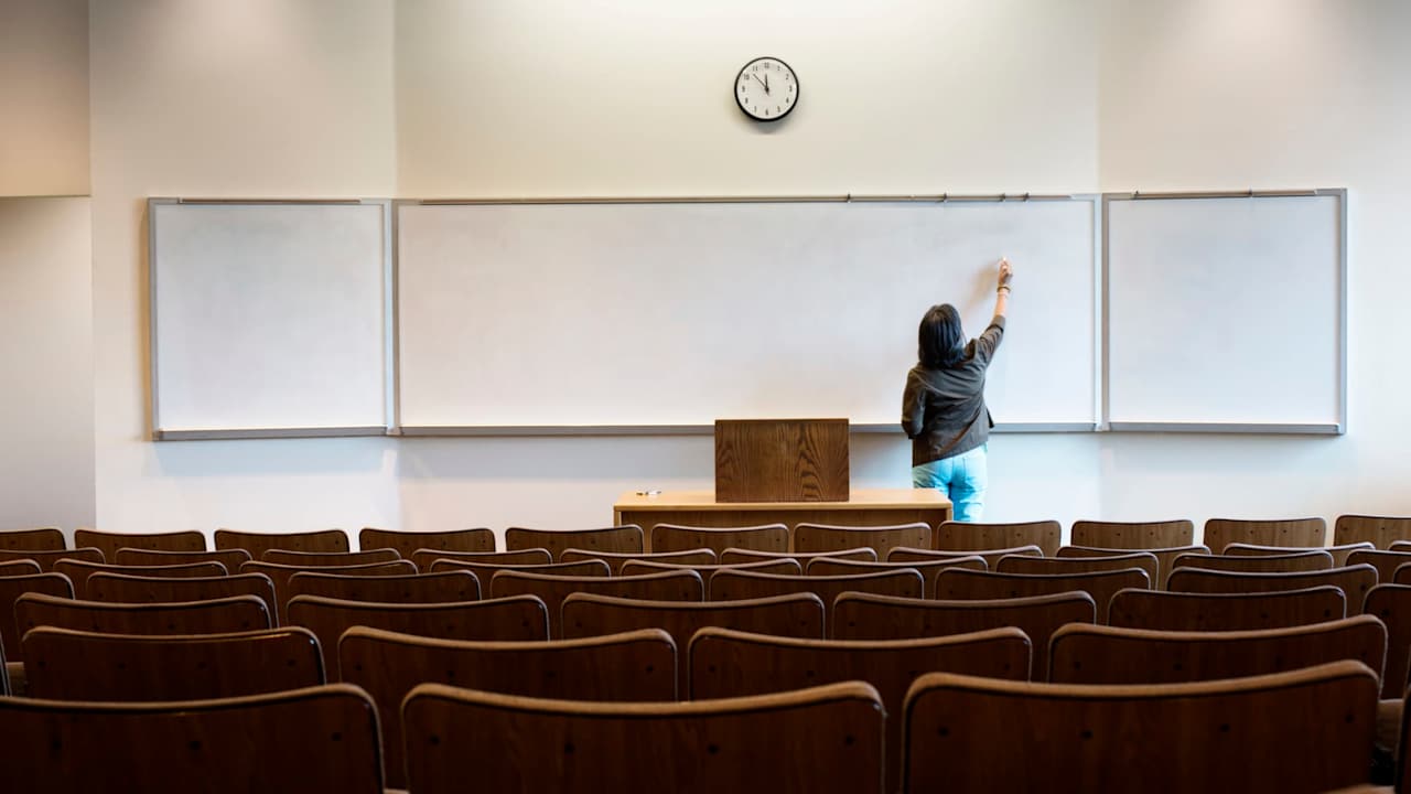 Female professor writing on whiteboard in an empty university lecture hall before class begins.