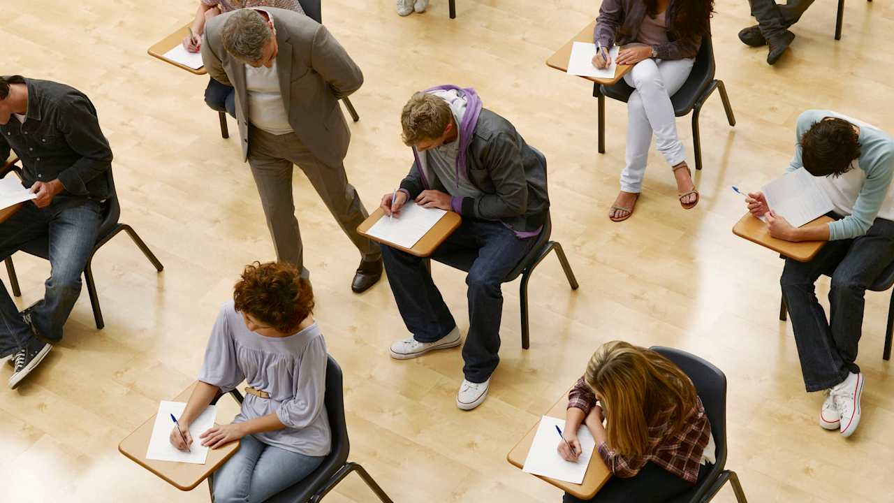 Teacher walking past high school students as he proctors an SAT exam session in a classroom.