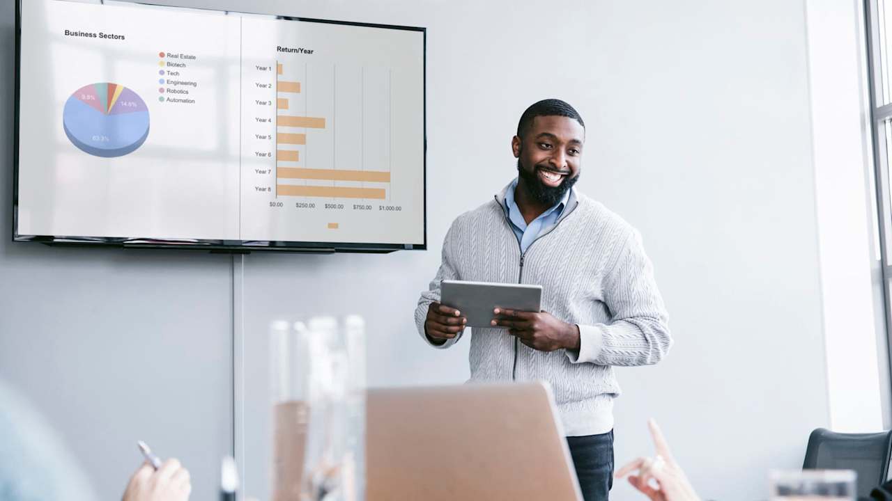 Smiling businessman holding tablet computer explaining graphs in meeting at board room