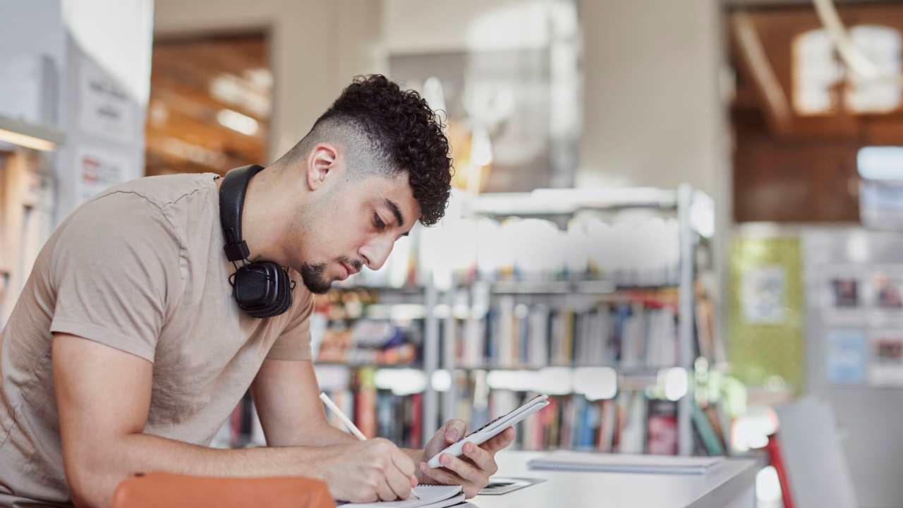 Male student taking notes in library.