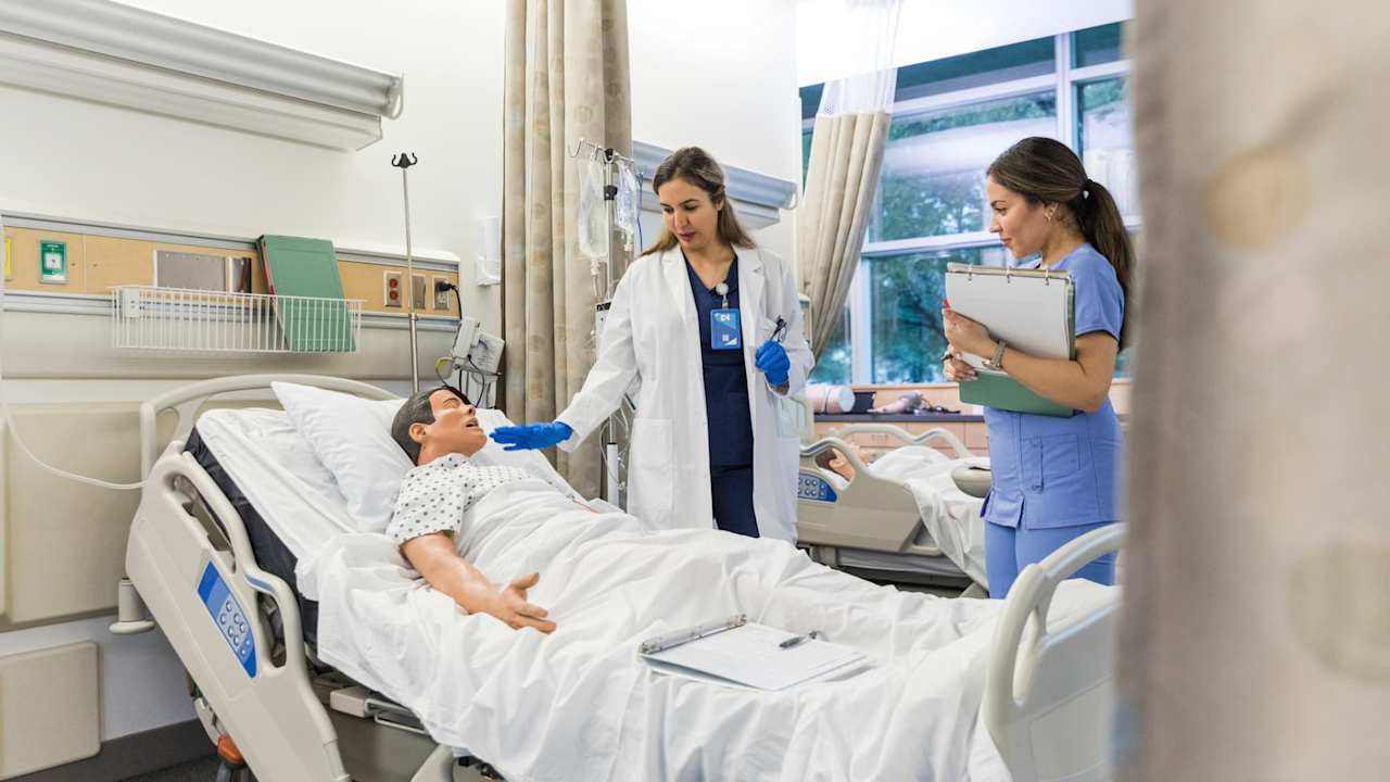 Nurses practicing on CPR dummy in hospital bed