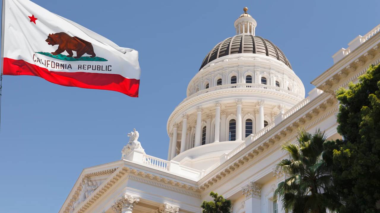 California State Capitol building with state flag in Sacramento on a windy summer day with clear sky.
