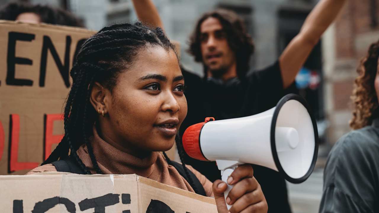 College students marching together in a protest against racism. Multi ethnic group of people in the city, they are holding cardboard signs.