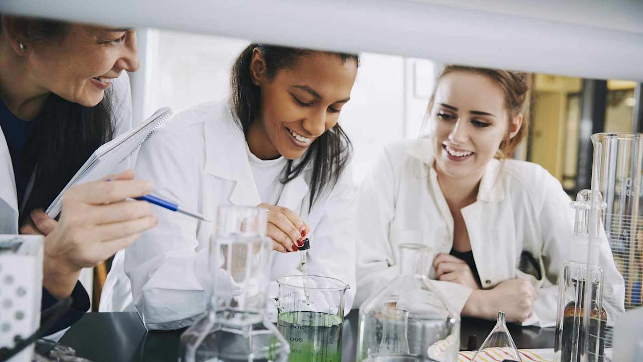 Smiling university students with mature teacher mixing solution in laboratory