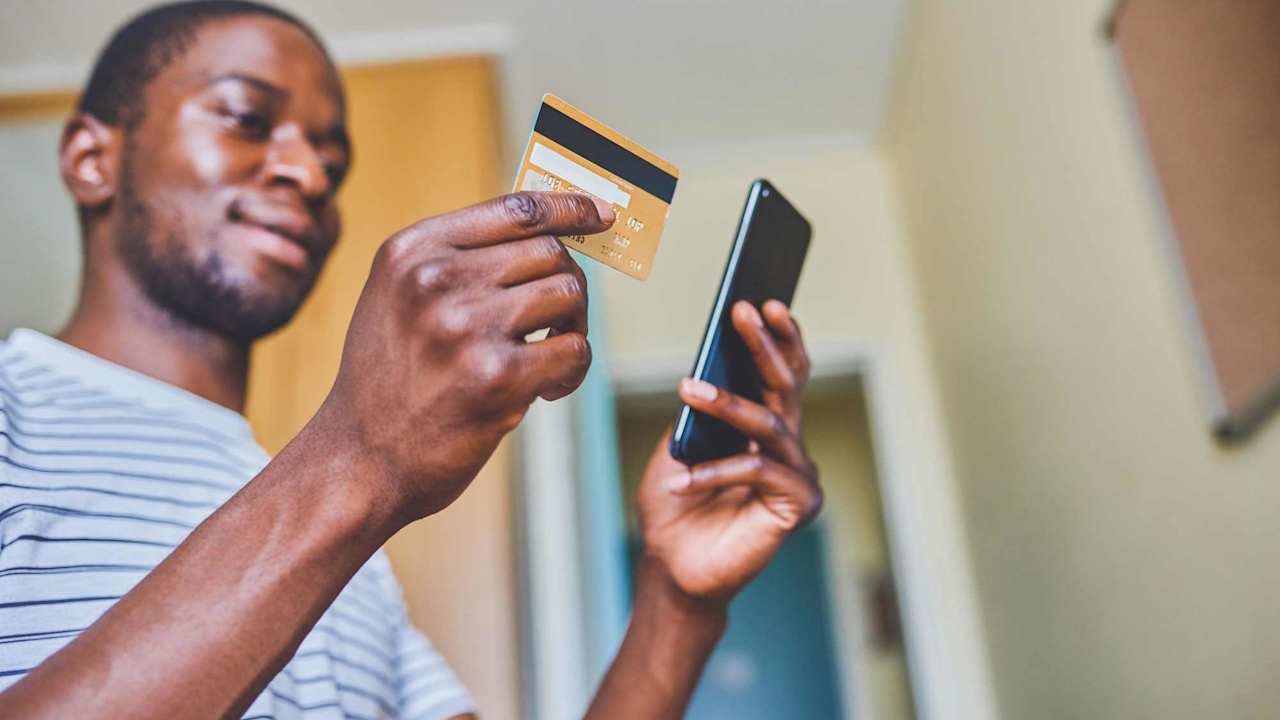 Cropped shot of a cheerful young man doing online shopping while using his cellphone and credit card inside of an apartment during the day