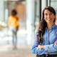 Smiling social worker standing in a hallway outside her office waiting to greet clients.