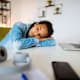 College Student at home with their head down on the desk looking out a window.