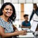 Portrait of mother working from home in residential kitchen with family in background