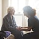 Registered nurse holding a senior patient's hands while sitting on her bed in her hospital room.