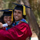 Two Indigenous students dressed in graduation gowns are smiling at the camera with their arms around each other.
