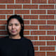 Indigenous college-aged woman standing against a brick wall.