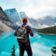 A hiker looks out at a bright blue lake in the mountains.