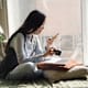 College student sitting on her bed in front of her laptop uses her credit card to pay an online bill.