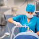 Asian American nurse anesthetist holding a mask in place over a patient's mouth before surgery.