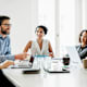 Business manager sitting at a large office desk talking to his employees during a morning meeting.