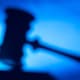 A faded silhouette of a judge's gavel resting on a bench in a courthouse.