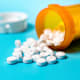 Drug tablets spilled onto a countertop from a prescription bottle.
