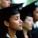 Black female graduate dressed in a cap and gown listens intently to a speaker at her college's commencement ceremony.