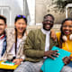 Happy and smiling group of multiracial college student friends looking at camera sitting on stairs outside university building.