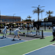 A group of people wearing white clothing playing pickleball on a bright sunny day.