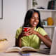 Young college student at home office taking lessons happily. Using laptop and books to investigate information about homework