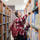 Female Asian American college student looking for textbooks on the shelves in her university's library.