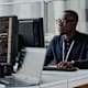 Black male cybersecurity engineer sitting at his desk in a corporate office. He is typing code for an internal security program on his desktop computer.