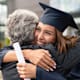 A smiling first generation college graduate hugs her father after receiving her degree during her commencement ceremony.