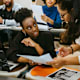 Black female student discussing a written assignment with her Black female teacher in the classroom.