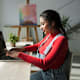 Latina student in red sweater sits at living room desk happy while working with her computer