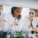 Smiling university students with mature teacher mixing solution in laboratory