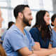 A group of medical school interns listen to a lecture by and unseen professor.