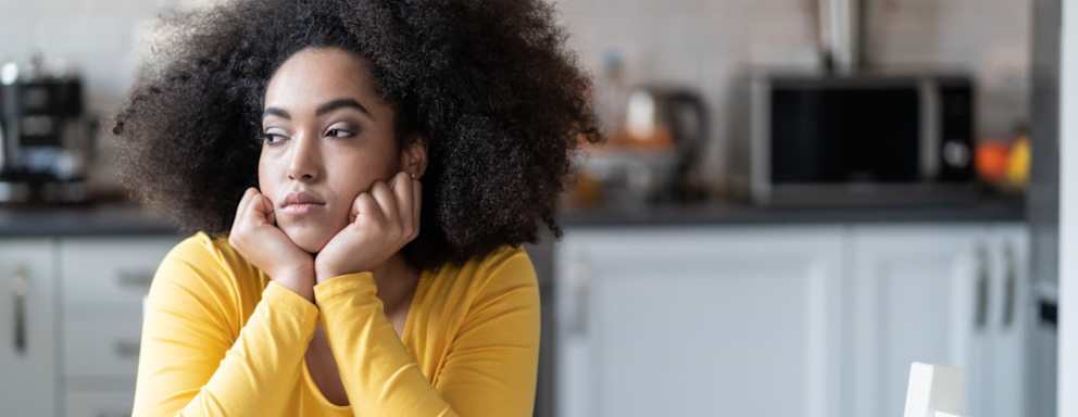 A depressed woman sitting at home alone in her kitchen looing sadly out of a window