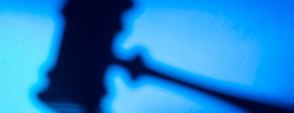 A faded silhouette of a judge's gavel resting on a bench in a courthouse.