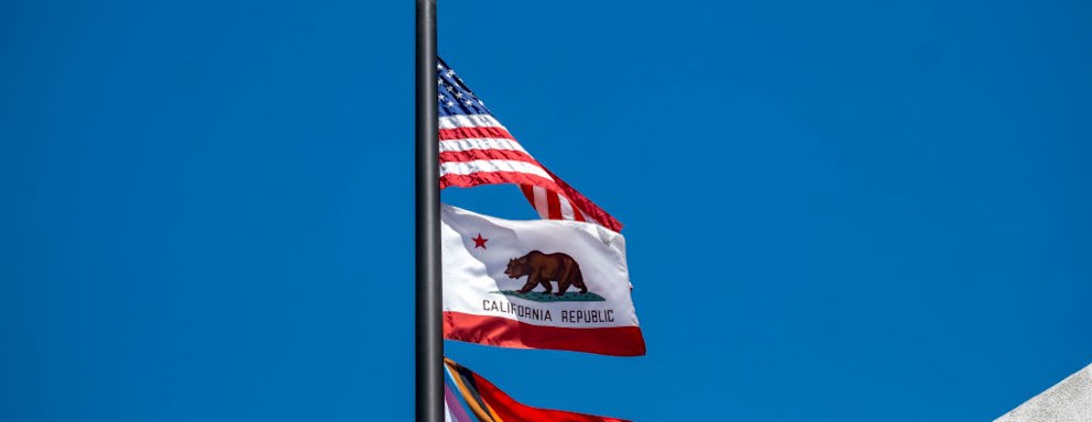 The U.S., California state, and rainbow pride flags wave in the wind during a Progressive Pride Flag raising ceremony at the city hall in San Fernando California.